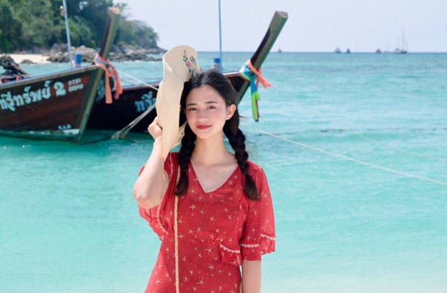 woman in red dress standing on beach of koh lipe in front of a long tail boat