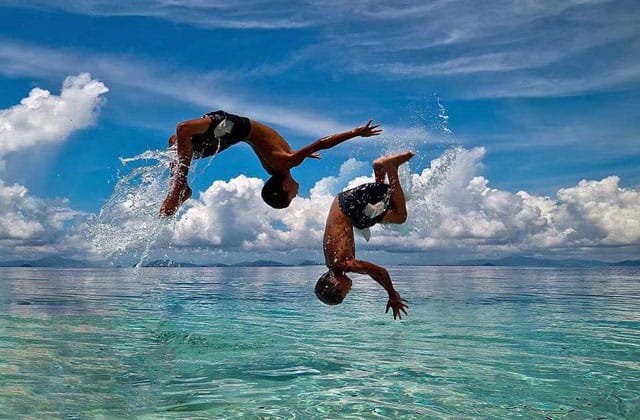 children in backpacker long house turn somersault above sea water in mabul island